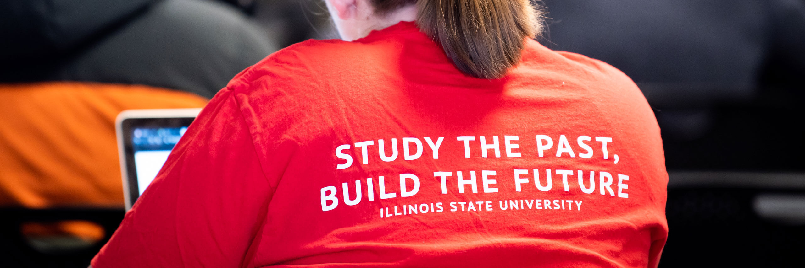 A student wears a shirt that reads 'Study the Past, Build the Future; Illinois State University'.